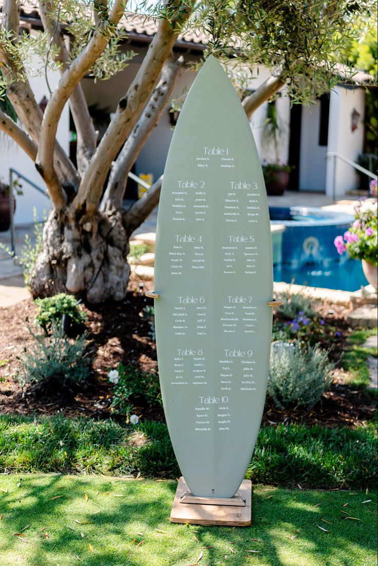 a surfboard is in the grass next to a tree and swimming pool with seating on it