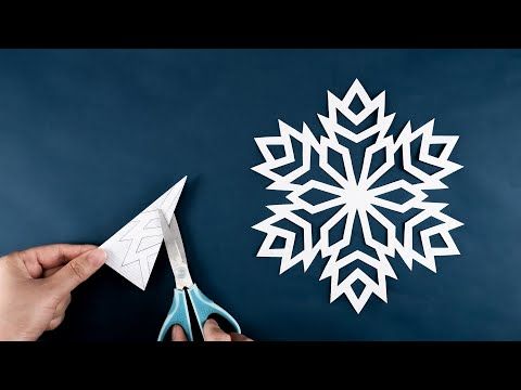 someone cutting out a paper snowflake on a blue background with scissors and glue