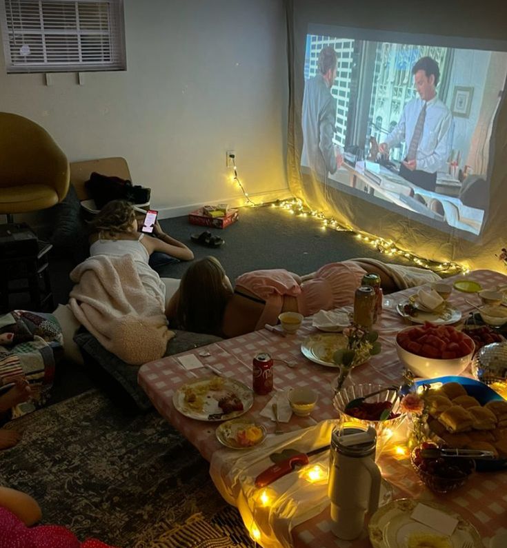 people sitting on the floor watching tv in a living room with food and drinks all around