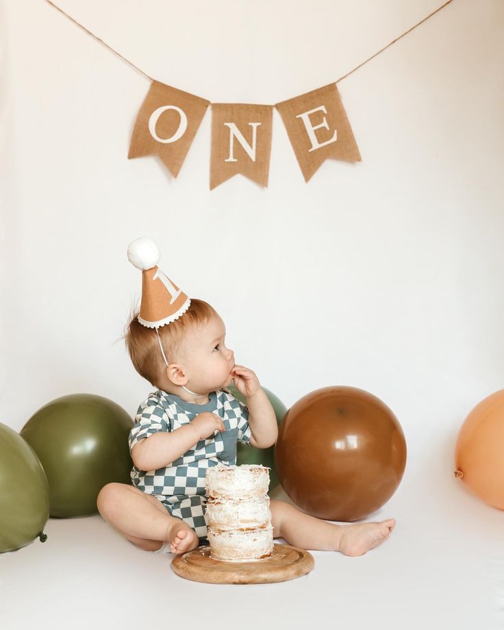 a little boy sitting on the floor with a cake and balloons in front of him