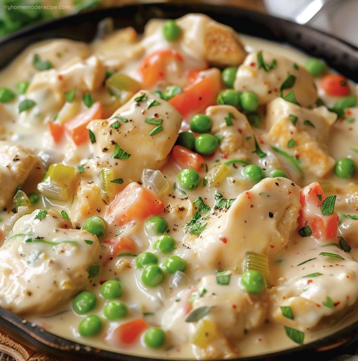 a skillet filled with chicken, peas and carrots on top of a table