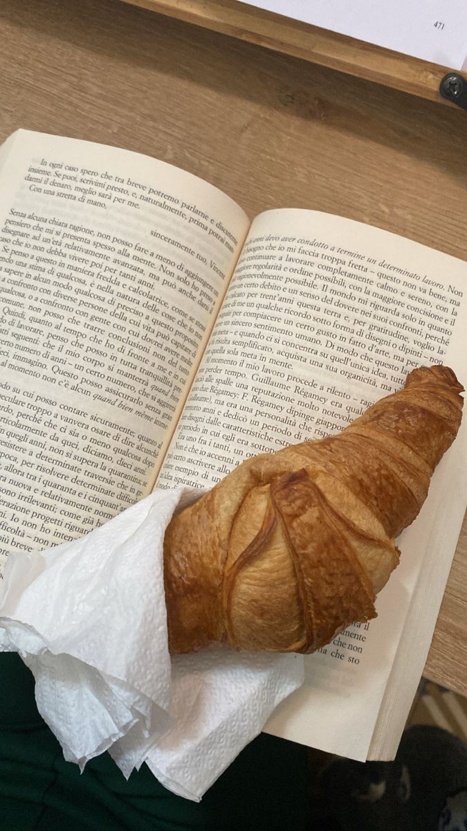 an open book on top of a table next to a croissant