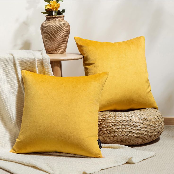 two yellow pillows sitting on top of a bed next to a vase with flowers in it