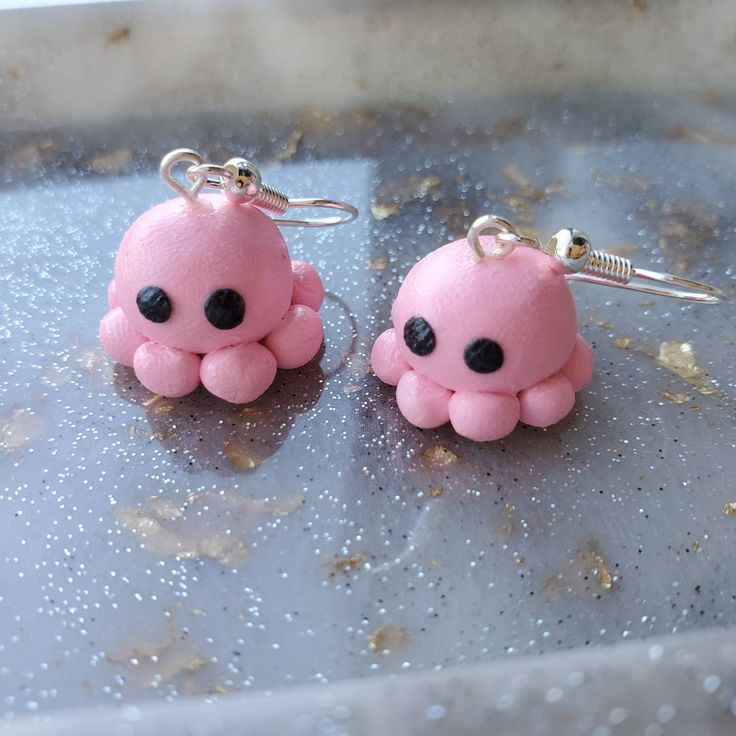 two pink octopus earrings with black eyes on a silver surface and gold flecks