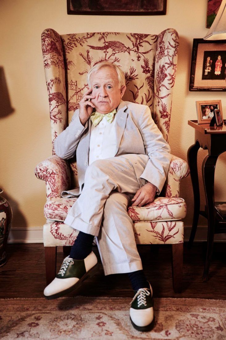 an old man sitting in a chair talking on the phone