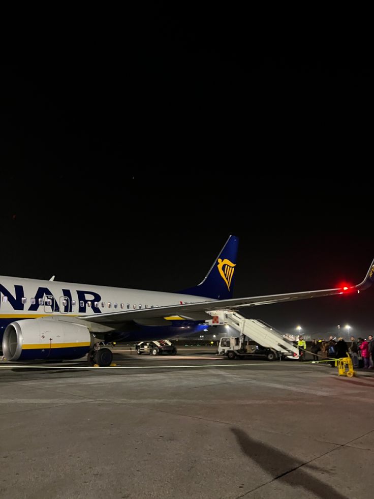 a large jetliner sitting on top of an airport tarmac at night with people standing around