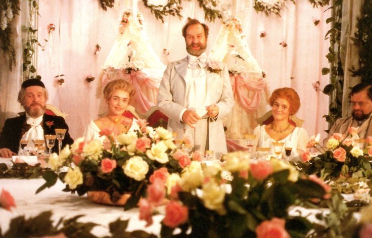 a group of people sitting at a table with flowers and candles in front of them