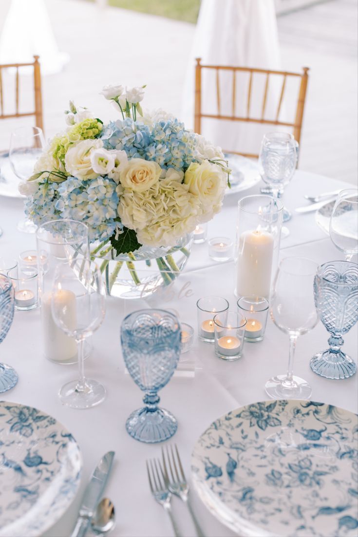 the table is set with blue and white dishes, silverware, candles, and flowers