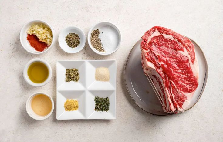 raw meat and seasonings arranged in bowls on a white counter top, including steak