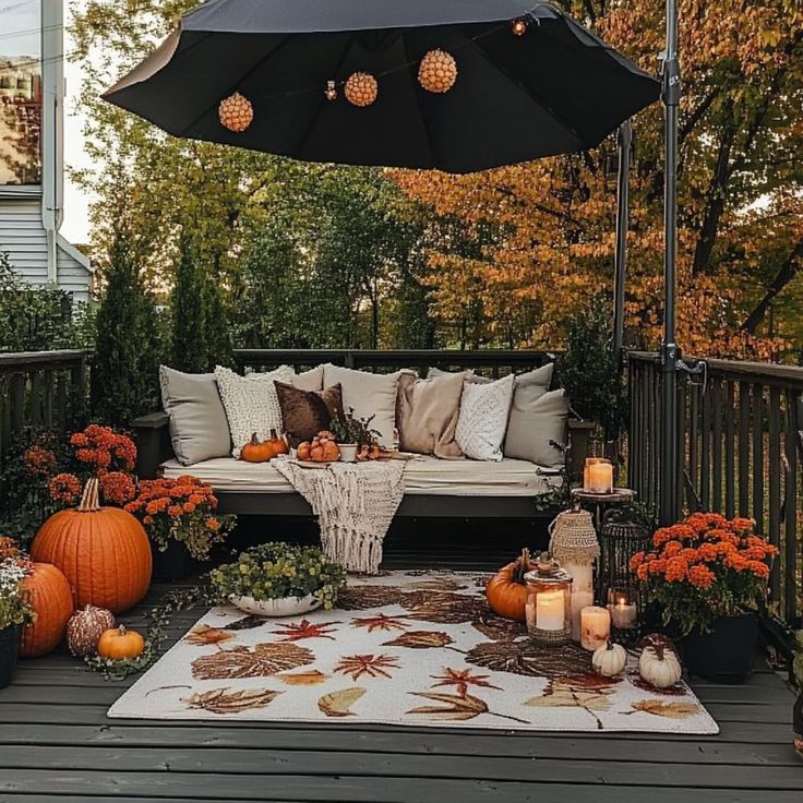 an outdoor patio decorated for fall with pumpkins, mumbers and candles on the deck