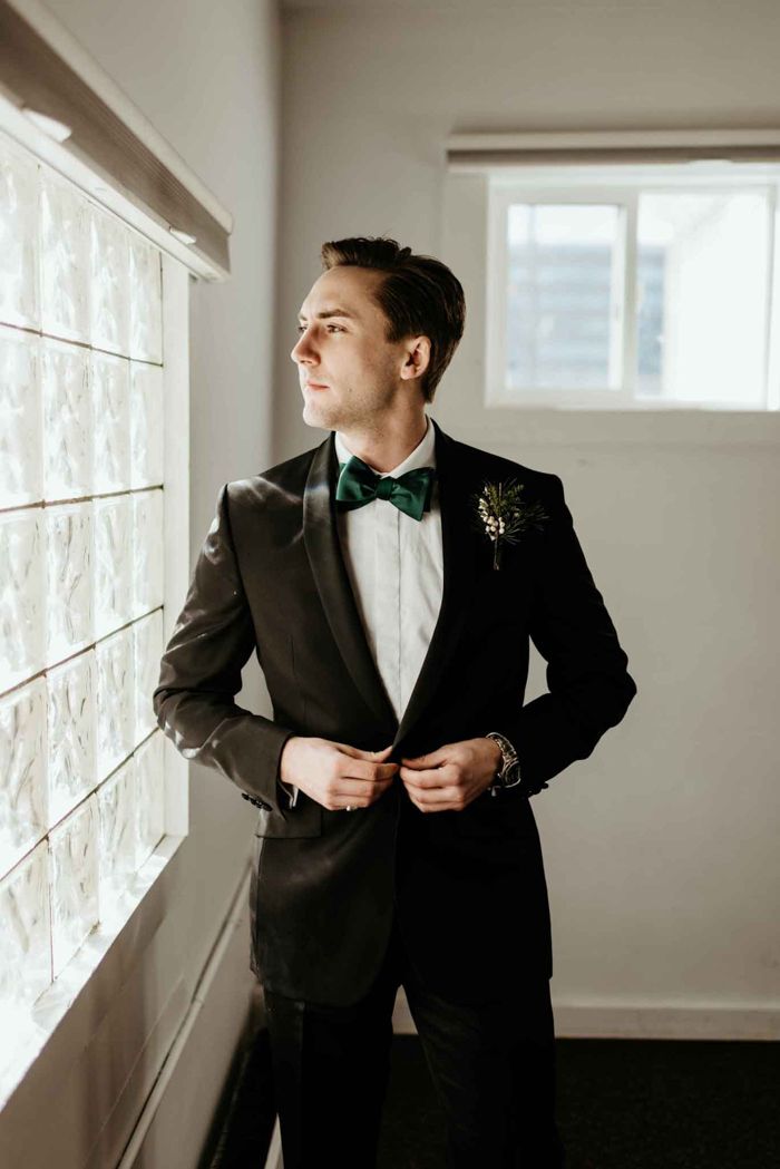 a man in a tuxedo standing next to a window