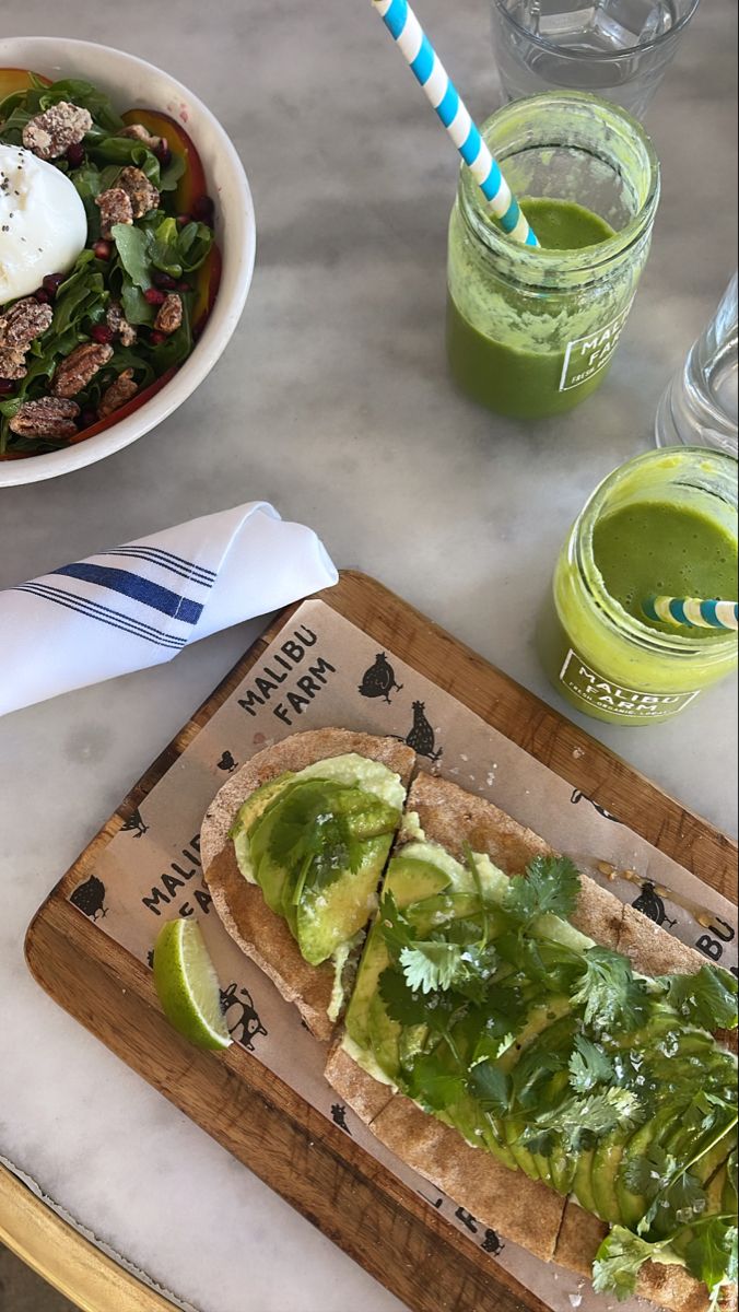 an open sandwich with avocado, meat and lettuce next to a bowl of green smoothie