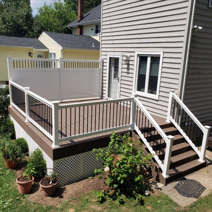 a deck with white railings in front of a house and some potted plants