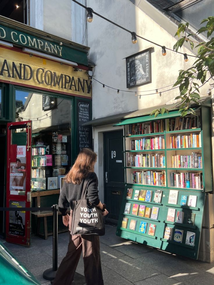 a woman is walking down the sidewalk in front of a book store with lots of books