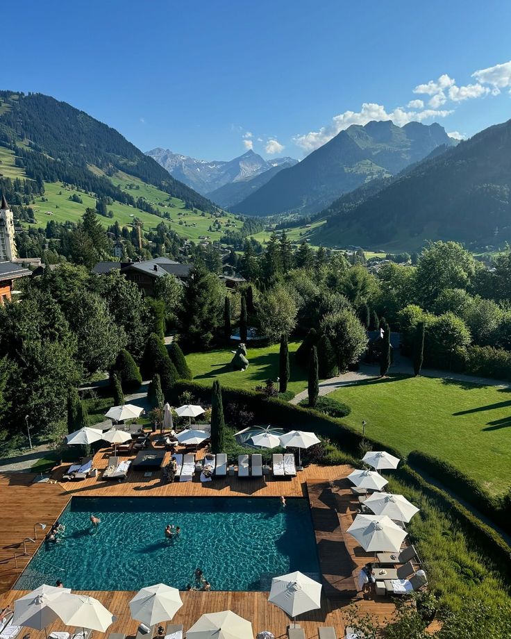 an aerial view of the pool and surrounding area with umbrellas, chairs and mountains in the background