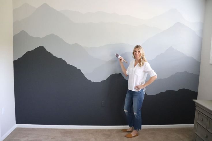 a woman standing in front of a wall with mountains painted on it and holding a camera