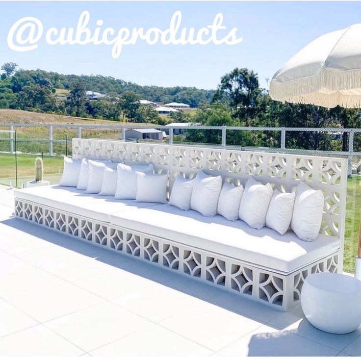 a white bench sitting on top of a lush green field next to a large white umbrella