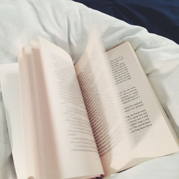 an open book sitting on top of a bed next to a white comforter and pillows