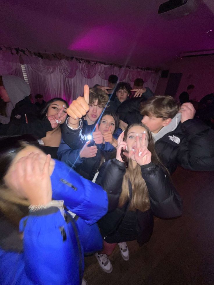 a group of young people taking pictures with their cell phones in a room filled with pink lights