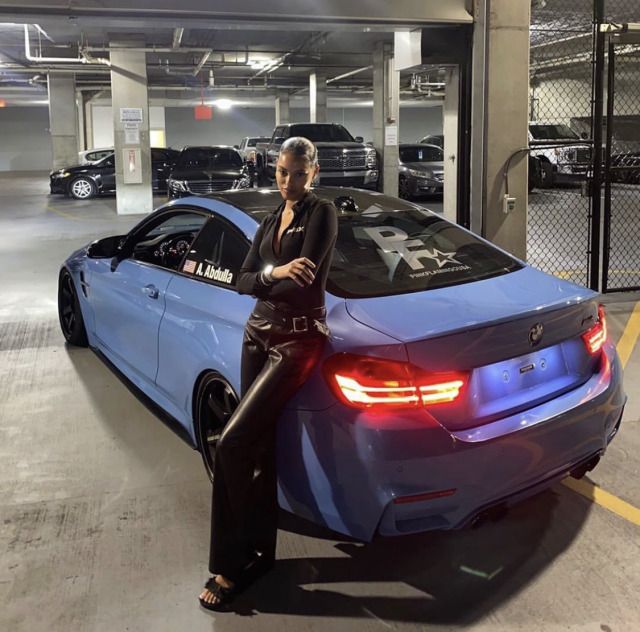 a woman sitting on the hood of a blue car in a parking garage next to other cars