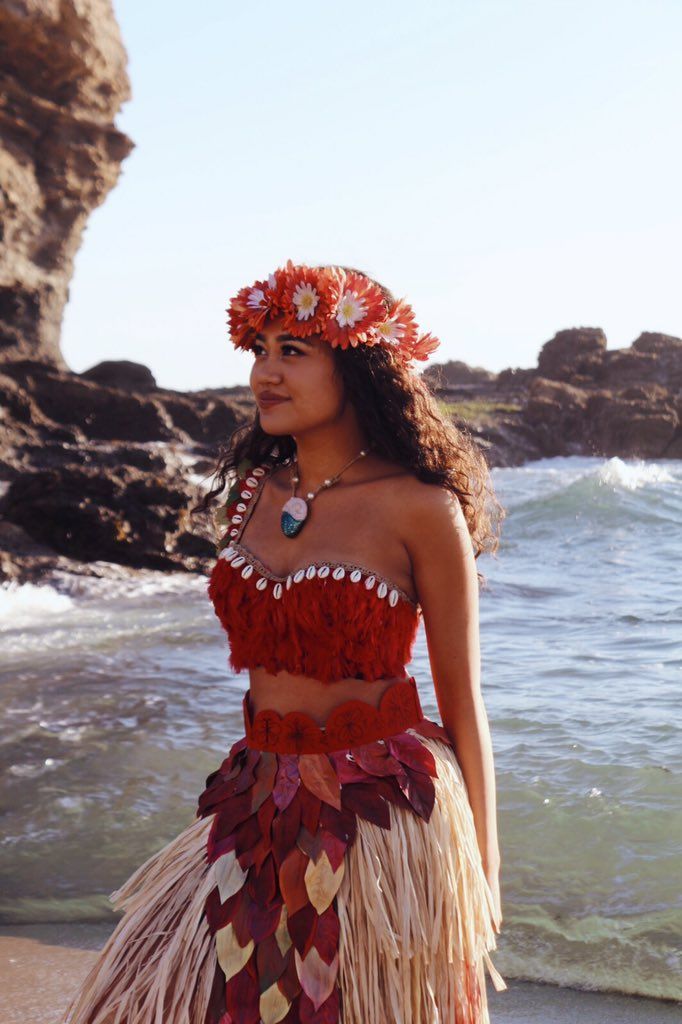 a beautiful young woman standing on top of a beach next to the ocean wearing a hula skirt