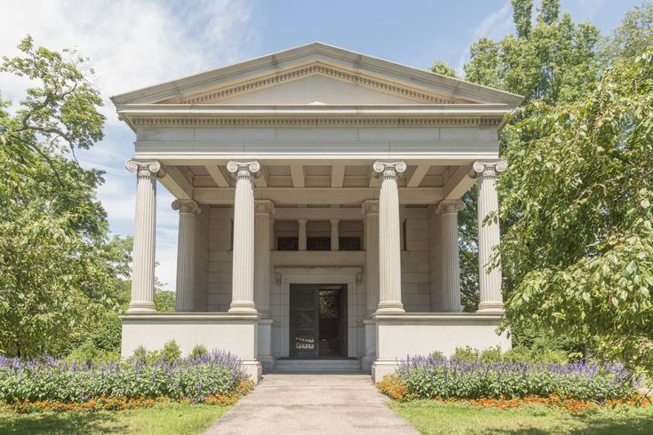 an old building with columns and pillars in front of it, surrounded by trees and flowers