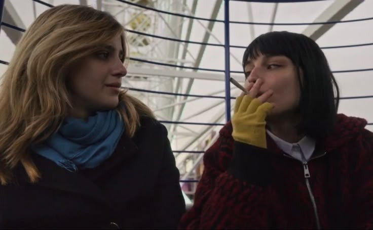 two women standing next to each other in front of a ferris wheel with one covering her mouth