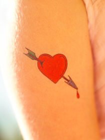 a red heart with an arrow tattoo on the left side of the arm and chest