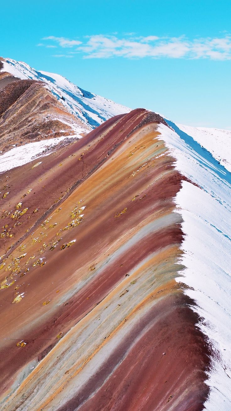 a mountain slope covered in colorfully colored rocks and grass with snow on the ground