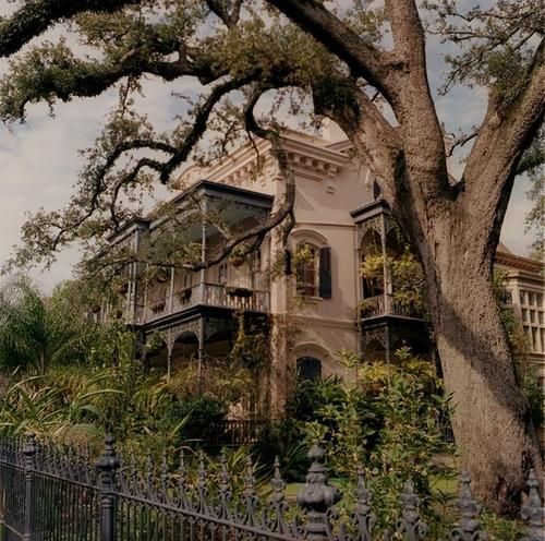 an old house with trees in front of it and a fence around the yard area