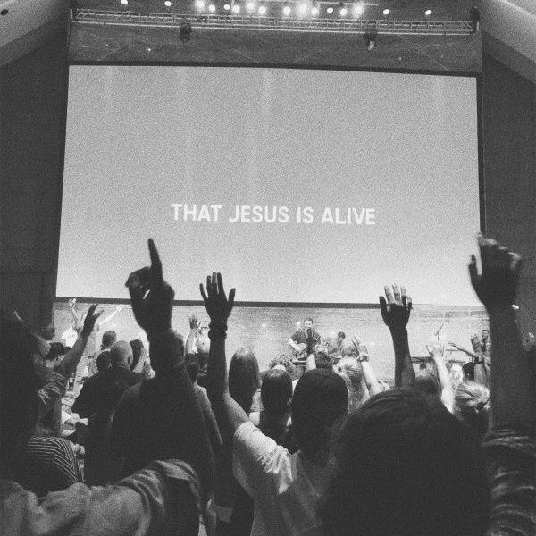 people raising their hands in front of a large screen with the words that jesus is alive on it