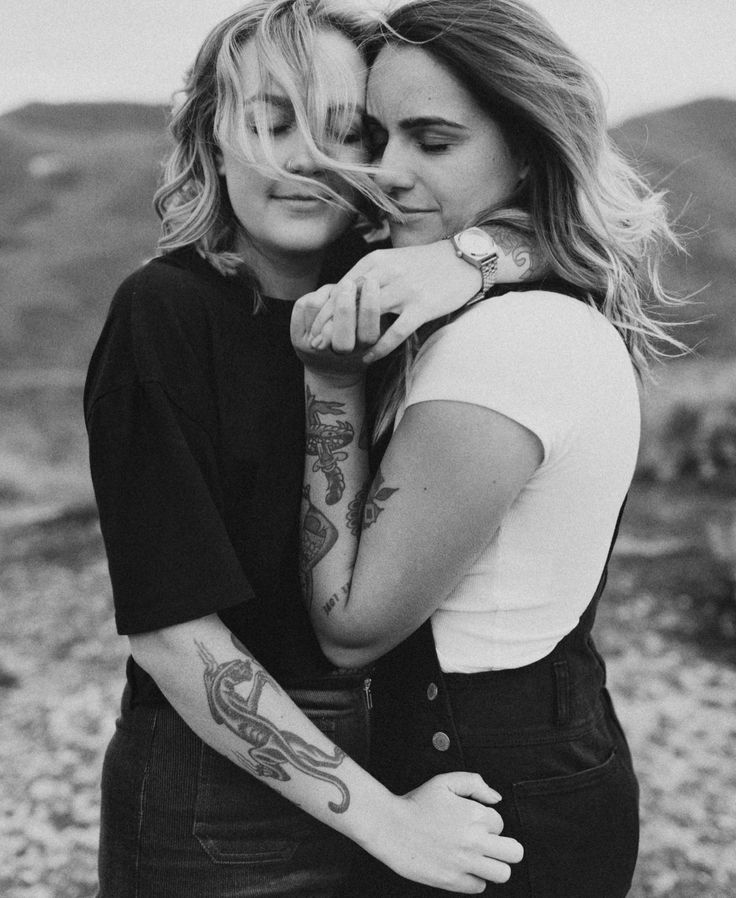 two women hugging each other in black and white with tattoos on their arms, one woman has her arm around the other's shoulder