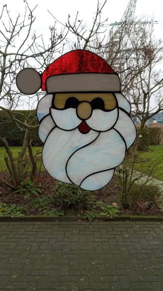 a stained glass santa claus face hanging from a brick walkway in front of a tree