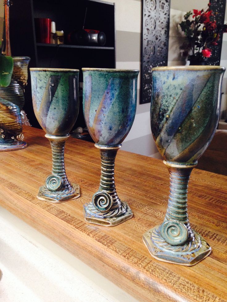 three wine goblets sitting on top of a wooden counter next to vases