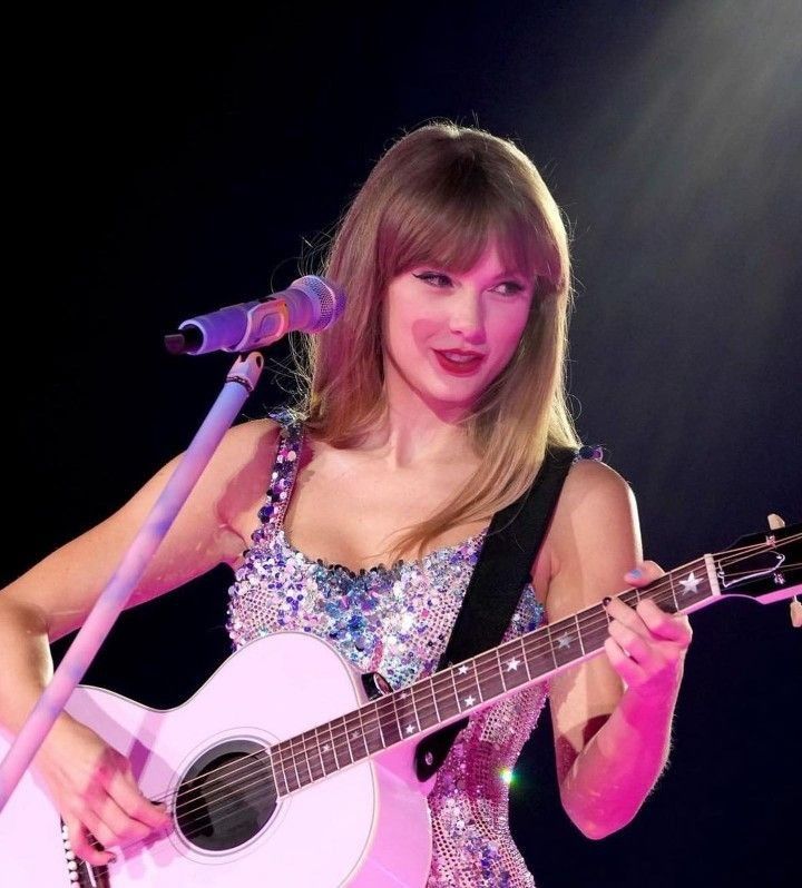 a woman holding a guitar and singing into a microphone