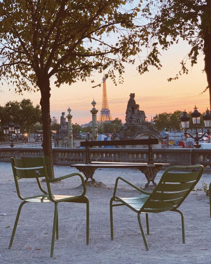 two green chairs sitting next to each other in front of a park with the eiffel tower in the background