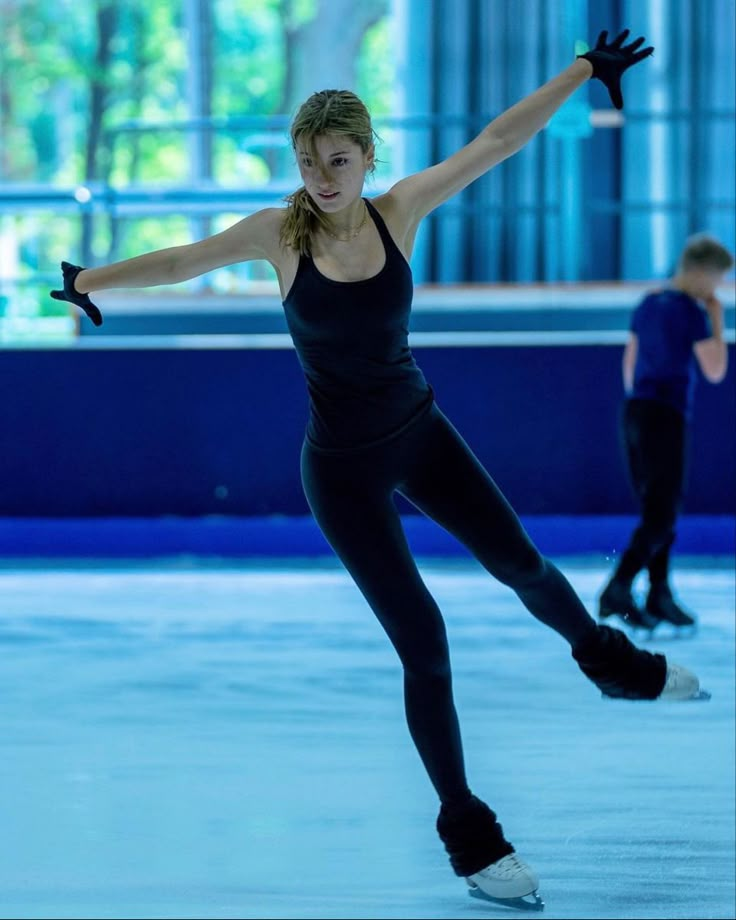 a woman skating on an ice rink in a black top and leggings with her arms outstretched