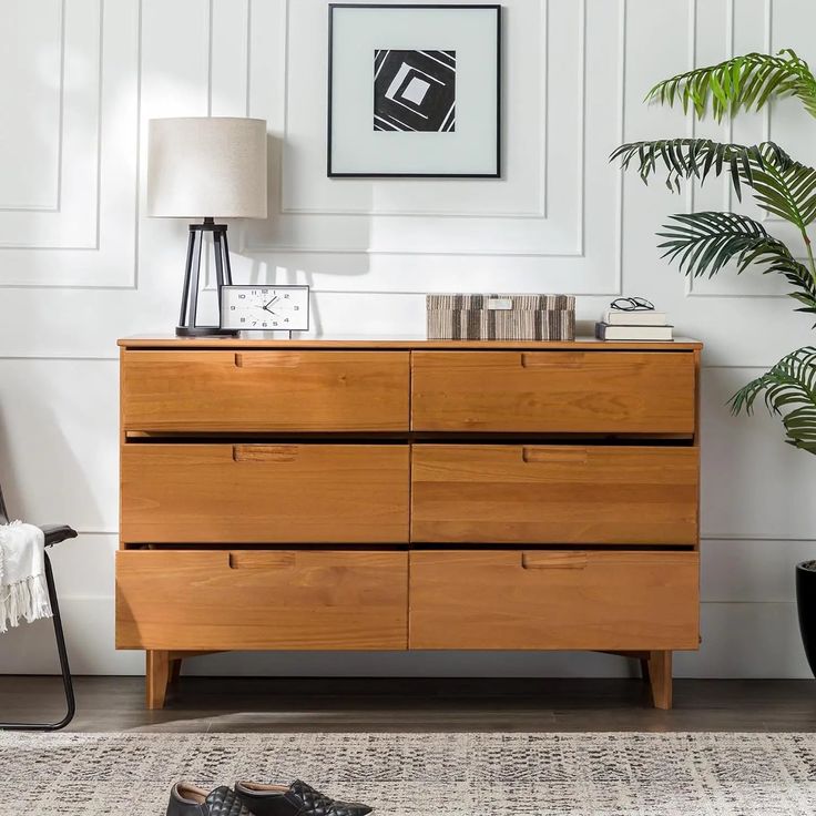 a wooden dresser sitting next to a plant in a living room on top of a rug