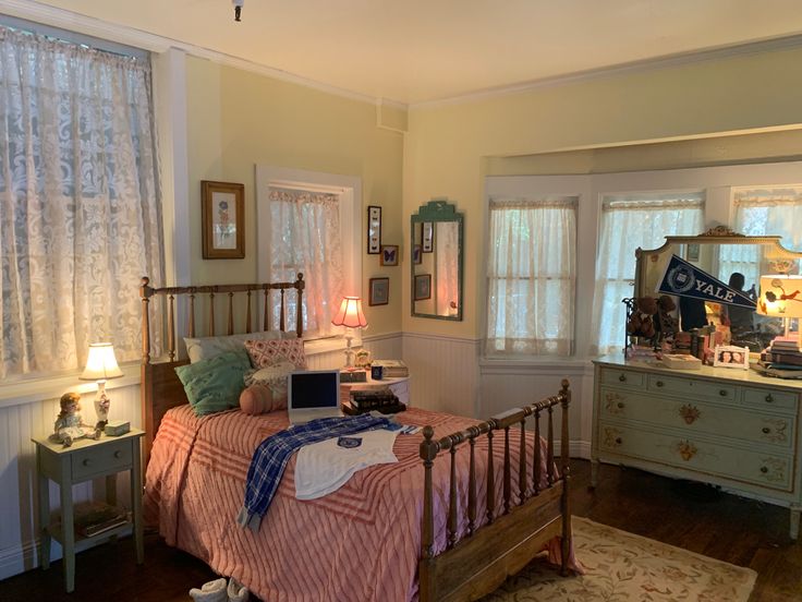 a bed room with a neatly made bed next to two windows and a laptop computer on top of the bed