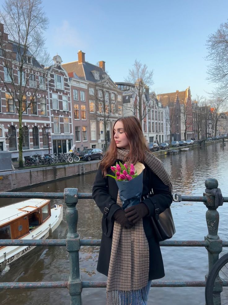 a woman is standing on a bridge with flowers in her hand and looking at the water