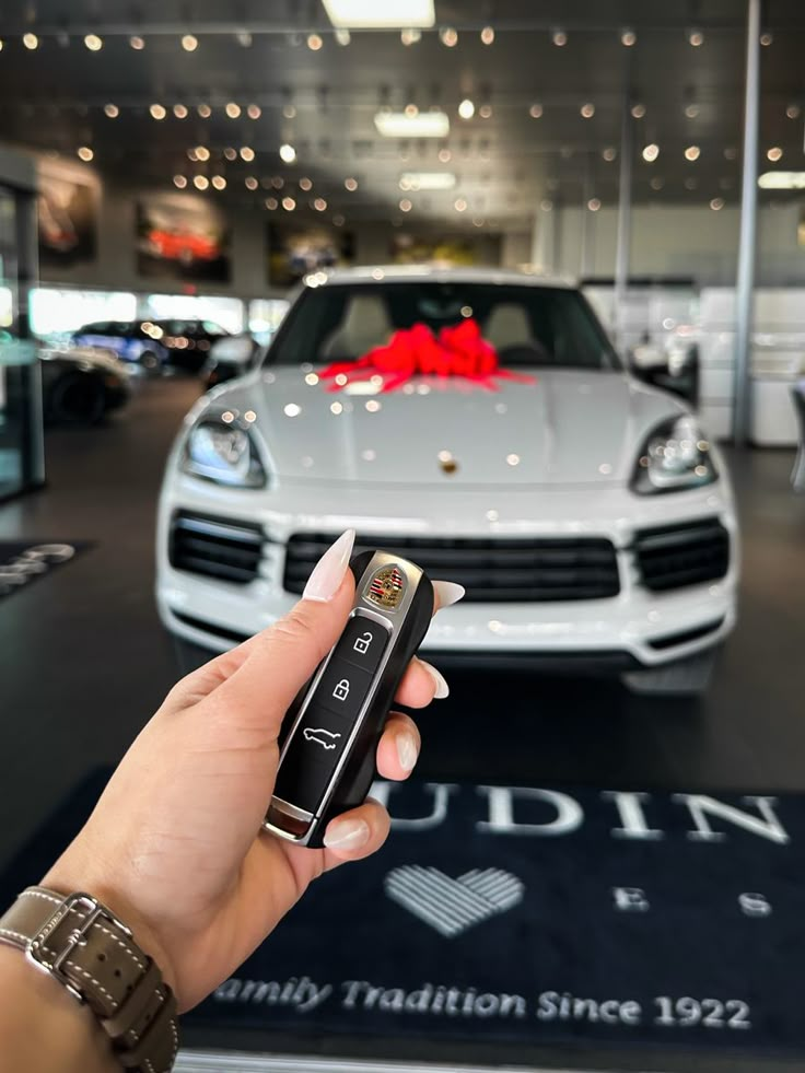 a hand holding a remote control in front of a white sports car at a showroom