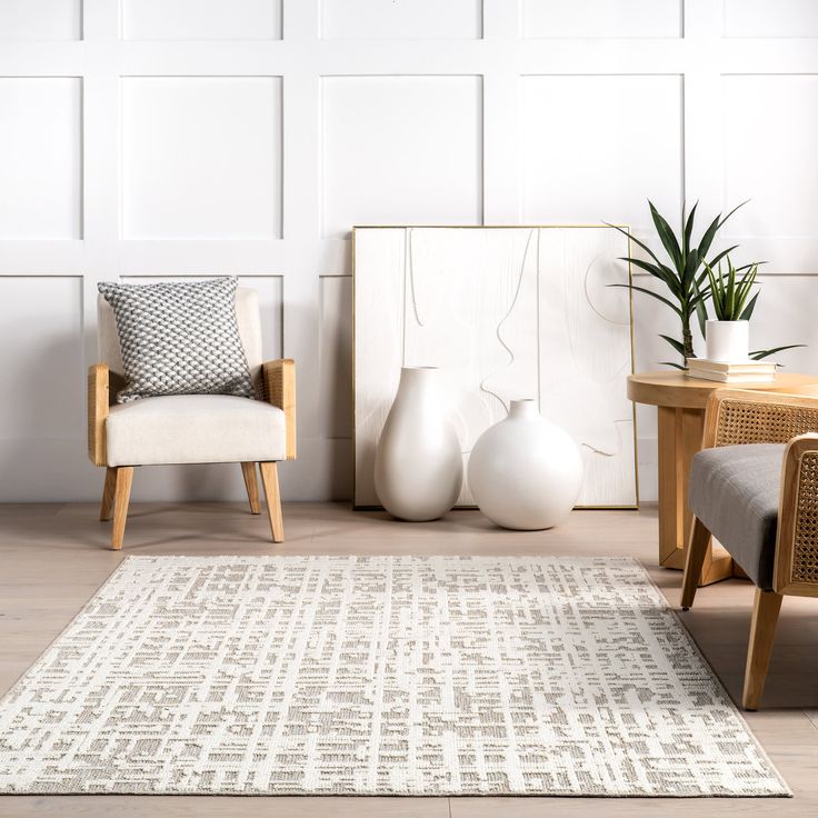 a living room with two chairs, a table and a rug in front of white paneled walls