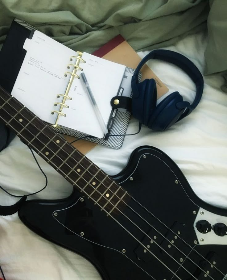 an electric guitar and headphones on a bed