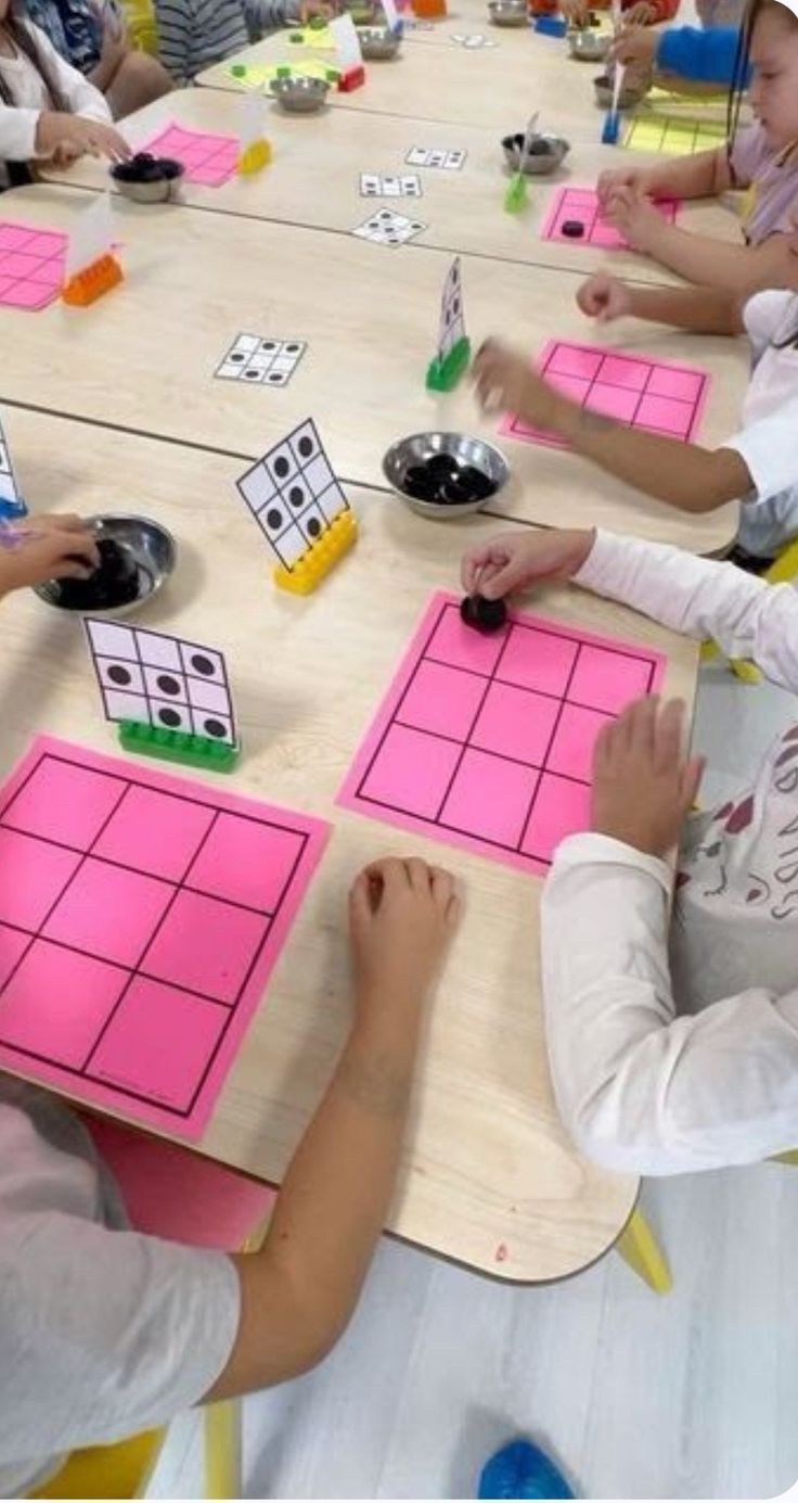 children are sitting at a table playing with pink squares