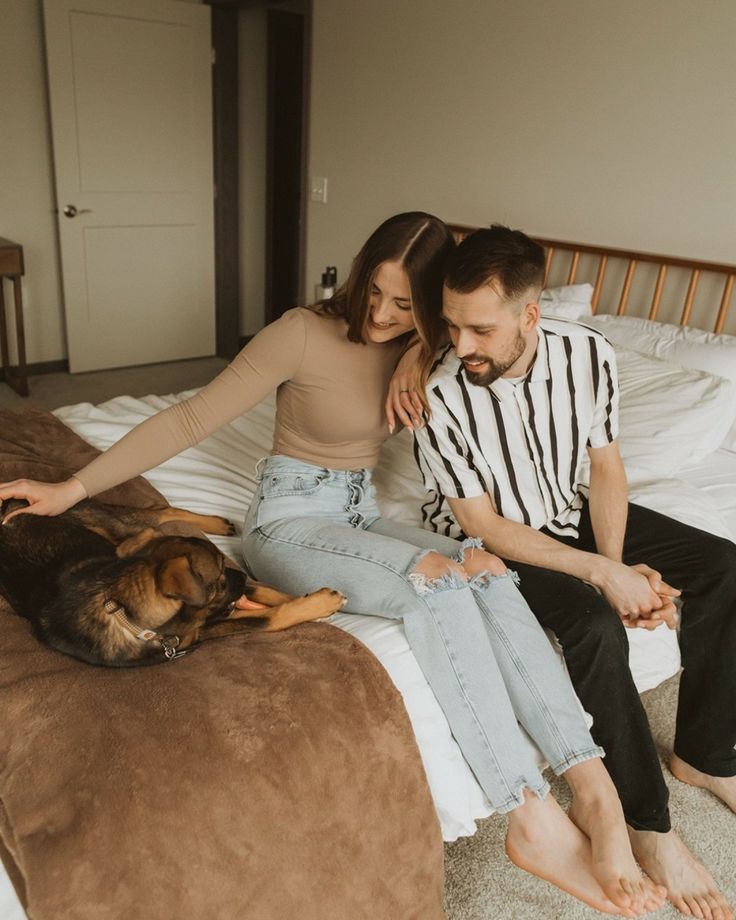 a man and woman sitting on a bed next to a dog