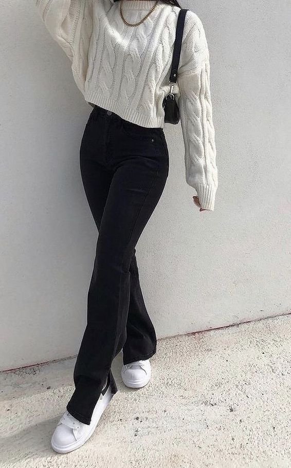 a woman in white sweater and black pants leaning against a wall with her hand on her head