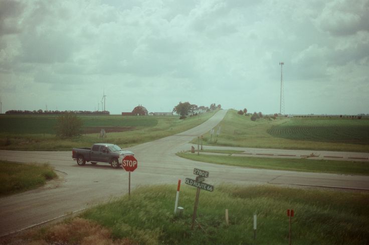 a truck driving down a rural road next to a stop sign and two street signs