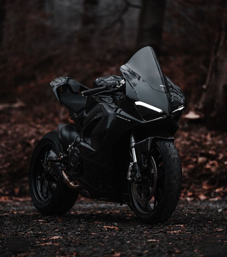 a black motorcycle parked on the side of a road in front of trees and leaves