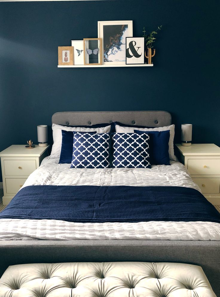 a bed with blue and white pillows in a bedroom next to pictures on the wall