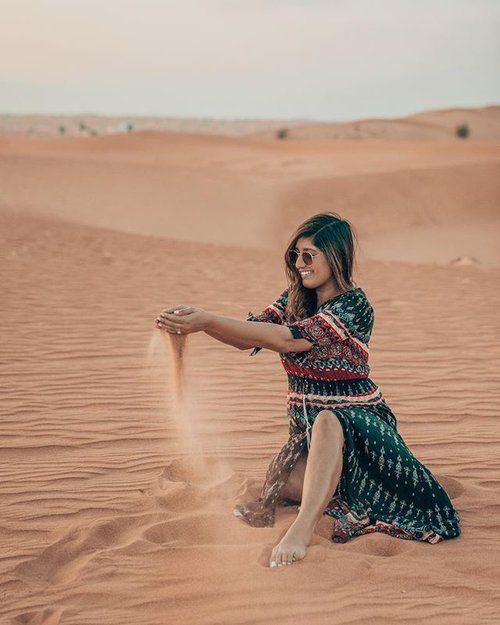 a woman sitting on top of a sandy beach next to a large sand dune in the desert